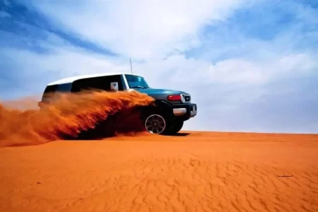 یک خودروی شاسی‌بلند در حال حرکت سریع در میان شن‌های کویر و ایجاد گرد و غبار زیر آسمان آبی
